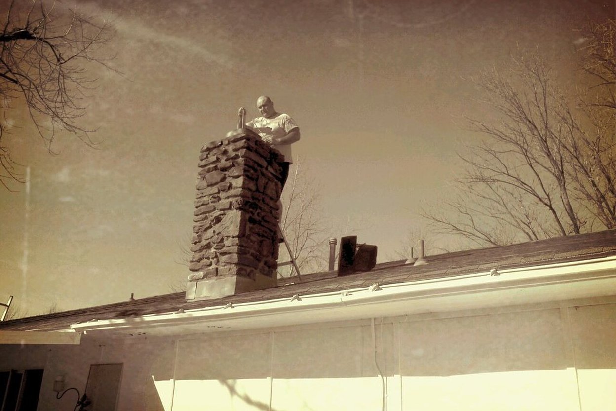 Man repairing stone chimney on house roof