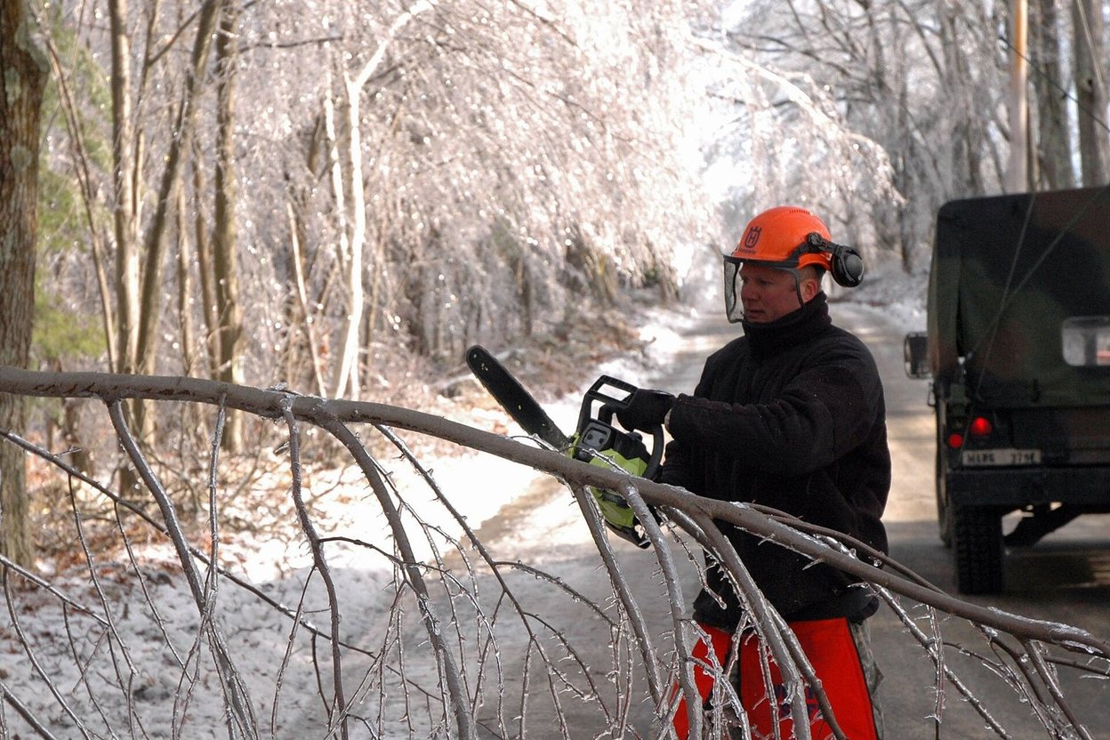 A soldier with a chainsaw clearing ice-covered fallen trees
